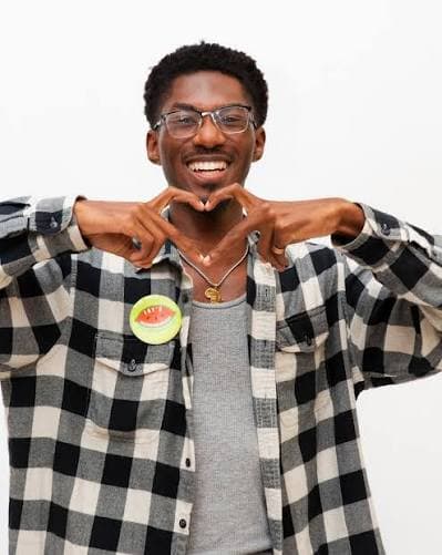 Joyson BaLisamore smiling and making a heart shape with his hands, wearing a plaid shirt and a watermelon pin.
