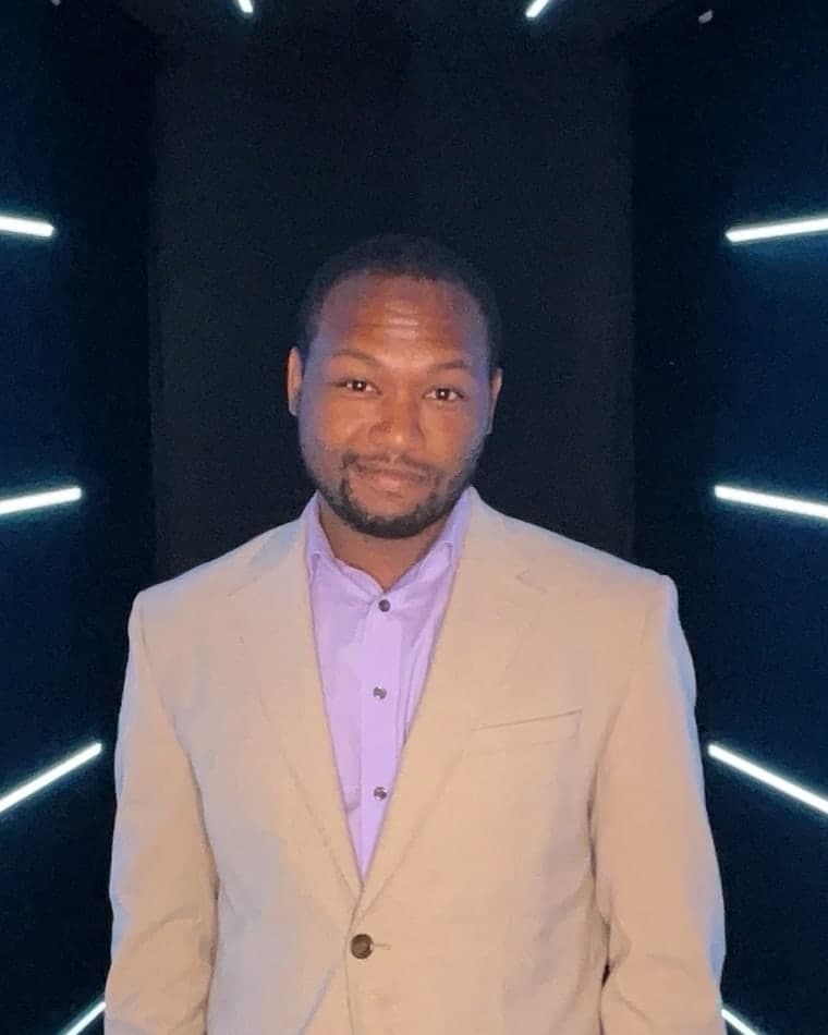 Jeffrey Scruggs in a tan blazer, standing in front of angled strips of white light.